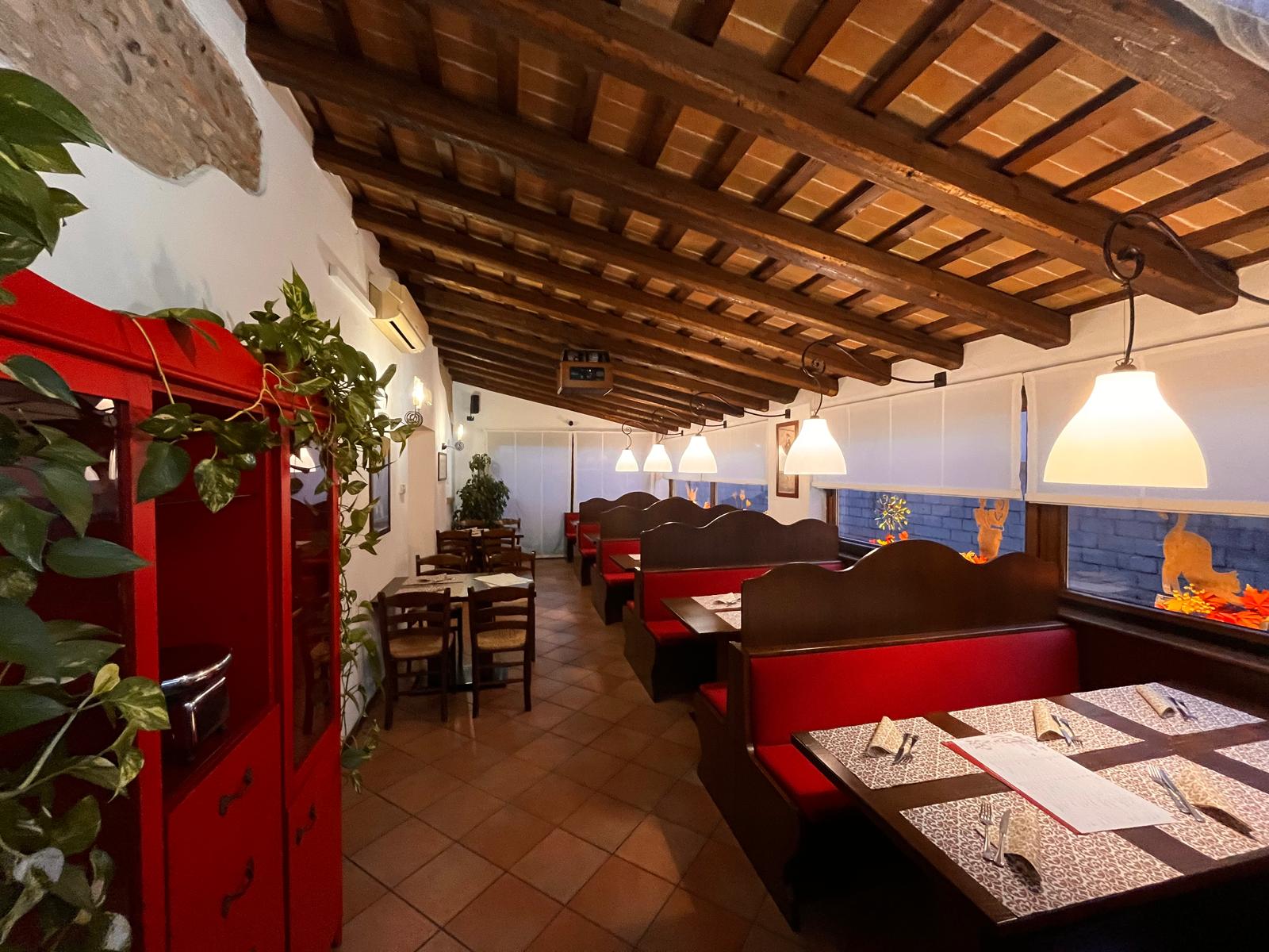 La sala di Pizzeria Agorà con le panche in legno, le sedute rosse e i tavoli apparecchiati